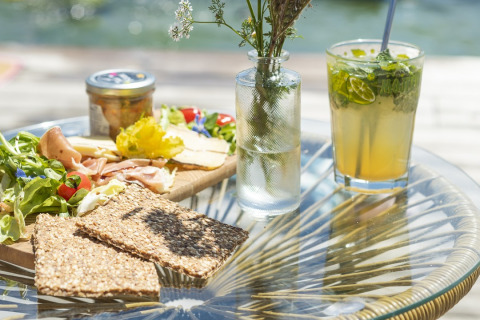 Ein köstlicher Outdoor-Snack mit Knäckebrot, Schinken, Käse, frischem Salat und einem erfrischenden Getränk.
