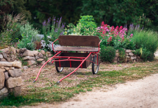 A wooden cart with red handles sits on a garden path at Dihan Evasion - Lodges Bretagne glamping site.