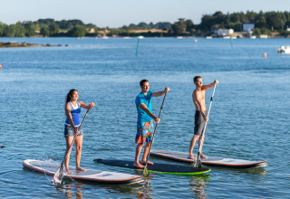 Tres personas practican paddle surf de pie sobre tablas en un lago junto a Dihan Evasion - Lodges Bretagne.
