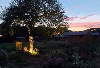 Vue du soir à Dihan Evasion - Lodges Bretagne, éclairage d’arbre et cabanes sous un ciel coloré.