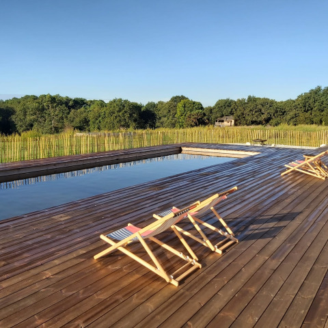 Terraza de madera con sillas reclinables junto a una piscina rodeada de naturaleza en Dihan Evasion - Lodges Bretagne.