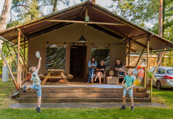 Family relaxing at Vakantiepark Ommerland – Safaritenten Overijssel glamping site while kids play outside.