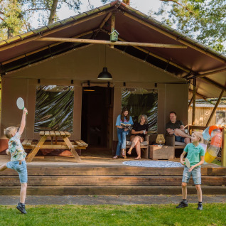 Familia se relaja frente a una tienda de lujo en Vakantiepark Ommerland – Safaritenten Overijssel; niños juegan.