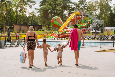 Famille allant vers la piscine au Vakantiepark Ommerland – Safaritenten Overijssel, toboggans colorés derrière.