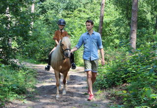 Man wandelt met kind op een paard door een bos bij Vakantiepark Ommerland – Safaritenten Overijssel.