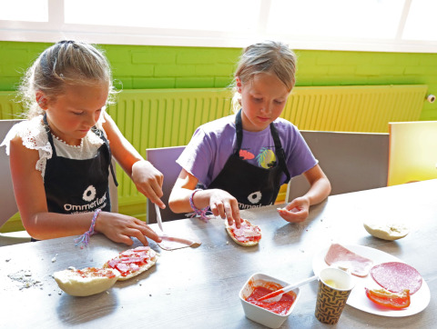 Twee kinderen bereiden samen eten aan een tafel in Vakantiepark Ommerland – Safaritenten Overijssel.