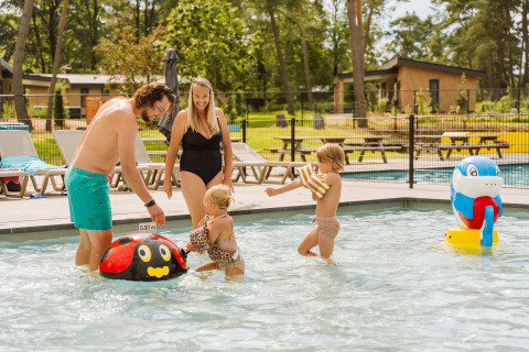 Famiglia si diverte nella piscina poco profonda sotto il sole al Vakantiepark Ommerland – Safaritenten Overijssel.