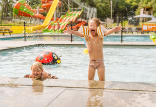 Two kids play and splash water in the children’s pool at Vakantiepark Ommerland with colorful slides visible.