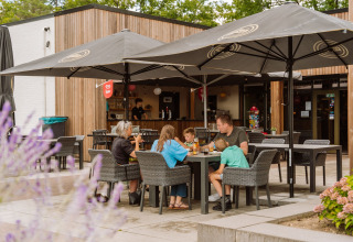 Familia comiendo al aire libre bajo grandes sombrillas en Vakantiepark Ommerland, alojamiento glamping Holanda.