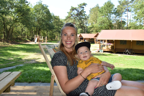 Moeder en baby ontspannen samen bij een safaritent op Vakantiepark Ommerland tussen het groen in Overijssel.
