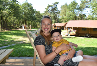 Mor og baby slapper af foran safaritelt ved Vakantiepark Ommerland, omgivet af natur og grønne områder.