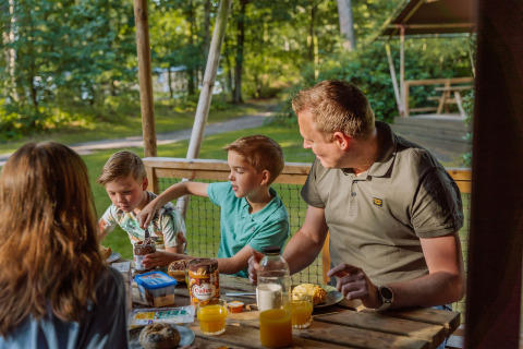 Familie nyder morgenmad udendørs i safaritelt på Vakantiepark Ommerland i Overijssel, Holland, omgivet af skov.