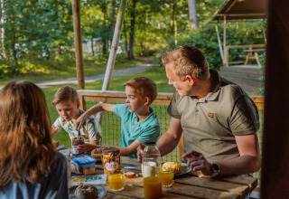 Famiglia fa colazione all'aperto in una tenda safari a Vakantiepark Ommerland, Overijssel, circondata dalla foresta.