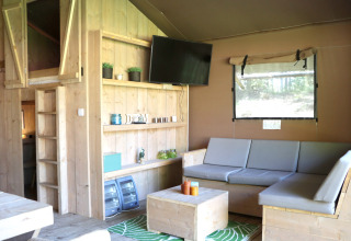 Intérieur d’une tente safari glamping au Vakantiepark Ommerland, Overijssel, avec meubles en bois et TV.