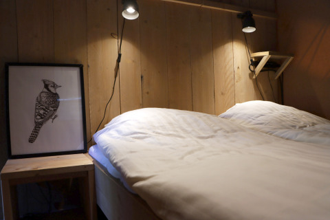 Gemütliches Glampingzimmer im Vakantiepark Ommerland mit Holzwänden, Doppelbett und Vogelbild.