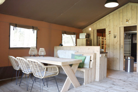Indendørs visning af en komfortabel glampingindkvartering med spisebord i træ i Vakantiepark Ommerland.