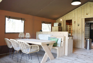 Binnenaanzicht van een sfeervolle safaritent met houten eettafel bij Vakantiepark Ommerland, Overijssel.