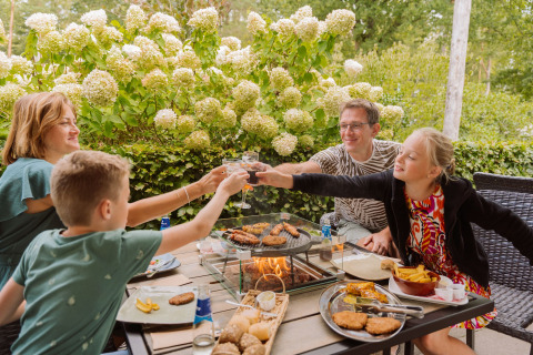 Familia disfruta de una comida al aire libre junto a la barbacoa en Vakantiepark Ommerland, Safaritenten Overijssel.