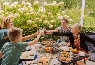 Gezin geniet van een barbecue buiten tussen de bloeiende struiken bij Vakantiepark Ommerland, Safaritenten Overijssel.
