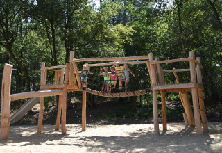 Bambini che giocano su un parco giochi in legno nella sabbia, circondati dalla foresta a Vakantiepark Ommerland Safaritenten Overijssel.