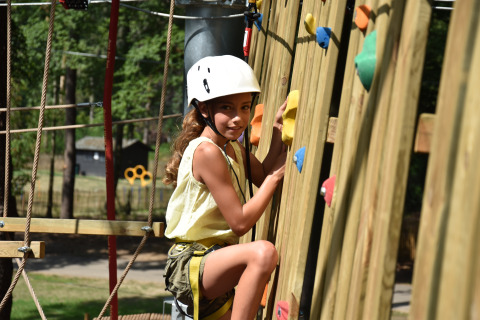 Child wearing a helmet climbs a rope adventure wall at Vakantiepark Ommerland – Safaritenten Overijssel.