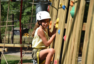 Kind met helm klimt op klimmuur bij Vakantiepark Ommerland – Safaritenten Overijssel.