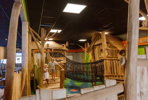 Zwei Kinder spielen auf einem Indoor-Spielplatz mit Holzhütten und Netzbrücke im Vakantiepark Ommerland – Safaritenten Overijssel.