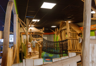 Dos niños juegan en un parque infantil cubierto con cabañas de madera y un puente de cuerda en Vakantiepark Ommerland – Safaritenten Overijssel.