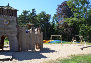 Aire de jeux pour enfants avec château en bois, balançoires et coussin sauteur coloré à Vakantiepark Ommerland.