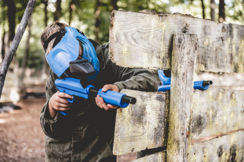 Bambino con maschera blu gioca a paintball dietro una staccionata al Vakantiepark Ommerland – Safaritenten Overijssel.