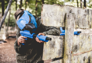 Barn iført blå maske og spiller paintball bag træhegn på Vakantiepark Ommerland – Safaritenten Overijssel.
