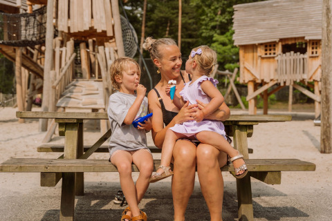 Madre con dos niños disfrutando helado en una mesa de picnic en Vakantiepark Ommerland – Safaritenten Overijssel.