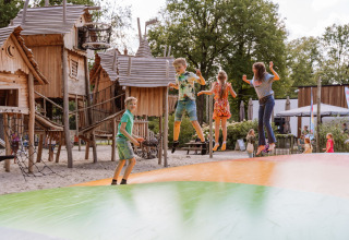 Børn leger på hoppepude foran træhytter på Vakantiepark Ommerland – Safaritenten Overijssel campingplads.