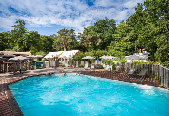 Piscina all'aperto presso Huttopia Douarnenez – Glamping Bretagne, circondata da lettini e verde boschivo.