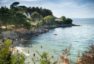 Blick auf den Strand und die Felsen bei Huttopia Douarnenez – Glamping Bretagne, Schwimmer im Wasser.