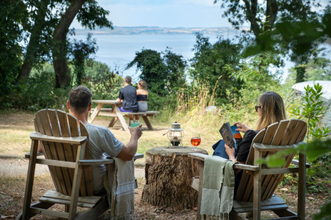 Parejas disfrutan del paisaje marino y forestal en Huttopia Douarnenez – Glamping Bretagne, sentados al aire libre.