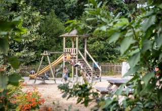 Legeplads omgivet af træer og buske på Huttopia Douarnenez – Glamping Bretagne, børnevenlig camping.