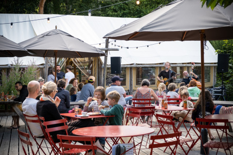 Area esterna di Huttopia Douarnenez – Glamping Bretagne con famiglie, sedie rosse e musica dal vivo.