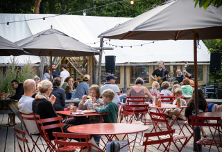 Terrasse extérieure de Huttopia Douarnenez – Glamping Bretagne, familles attablées et concert de musique live.