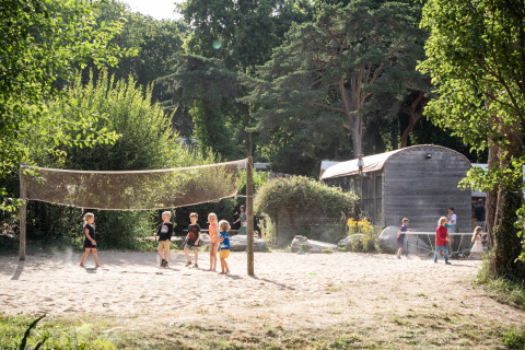 Children play on a sandy area at Huttopia Douarnenez glamping, surrounded by nature and trees.