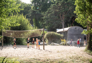 Kinderen spelen in het zand bij glamping Huttopia Douarnenez, omringd door bomen en natuur.