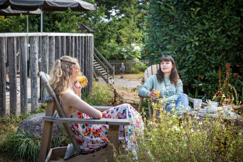 Zwei Frauen entspannen sich mit Getränken im Garten bei Huttopia Douarnenez – Glamping Bretagne.
