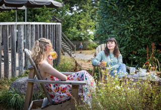 To kvinder nyder en drink i haven ved Huttopia Douarnenez – Glamping Bretagne under afslappede forhold.