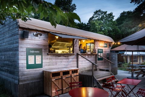 Outdoor wooden café-restaurant at Huttopia Douarnenez – Glamping Bretagne, with terrace seating at dusk.