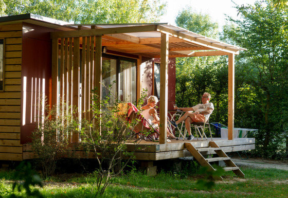 Due persone si rilassano sulla veranda soleggiata del glamping Huttopia Saumur in Pays de la Loire.