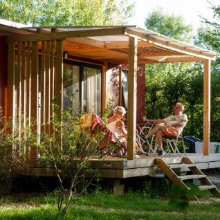 Dos personas se relajan en la terraza de madera soleada de Huttopia Saumur, glamping en Pays de la Loire.