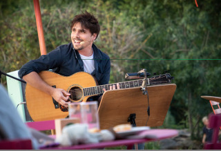 Musician performs with acoustic guitar outdoors at Huttopia Saumur - Glamping Pays de la Loire, near nature.