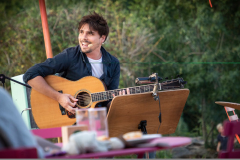 Muzikant speelt gitaar bij Huttopia Saumur - Glamping Pays de la Loire, genietend van een sfeervolle natuur.