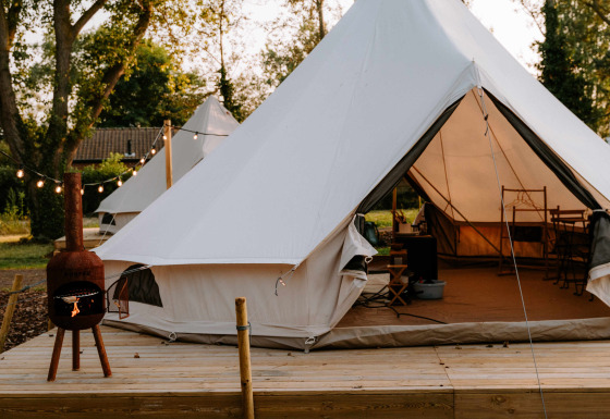 Glampingtenten van Boszee in West-Vlaanderen met houten terras en gezellige avondverlichting.