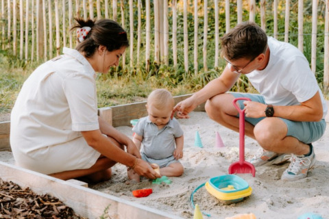 Gezin speelt in de zandbak bij Boszee - Glampingtenten West-Vlaanderen, omgeven door natuur.